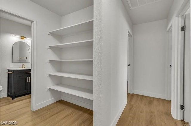 hall with light wood finished floors, baseboards, and a sink