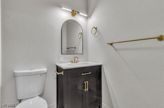 half bath with toilet, vanity, and a textured wall