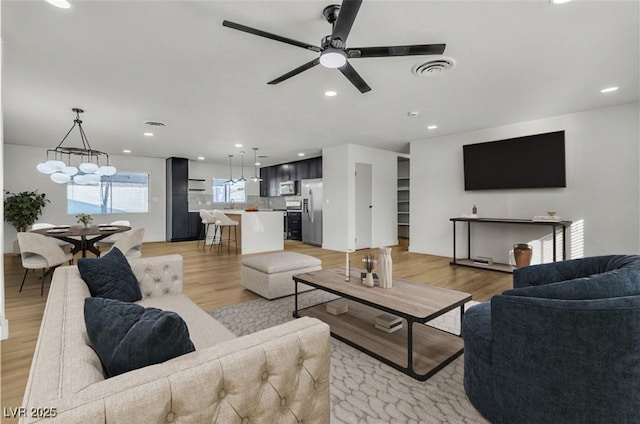 living room featuring light wood-type flooring, ceiling fan with notable chandelier, visible vents, and recessed lighting