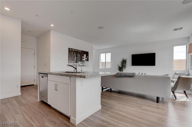 kitchen with stainless steel dishwasher, visible vents, a sink, open floor plan, and a center island with sink