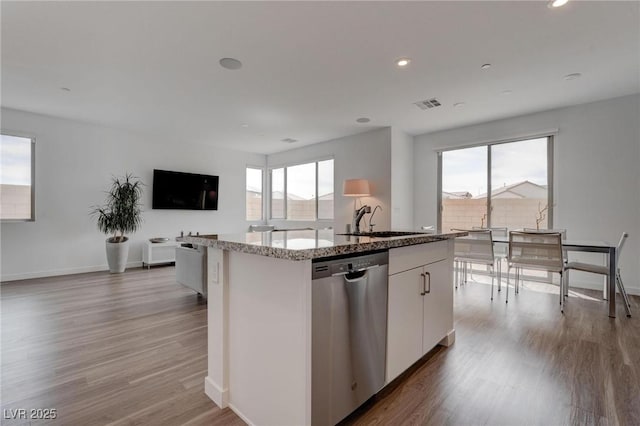 kitchen with visible vents, a sink, a kitchen island with sink, light stone countertops, and stainless steel dishwasher