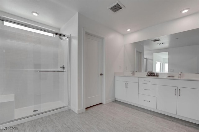 full bath featuring a stall shower, double vanity, a sink, and visible vents