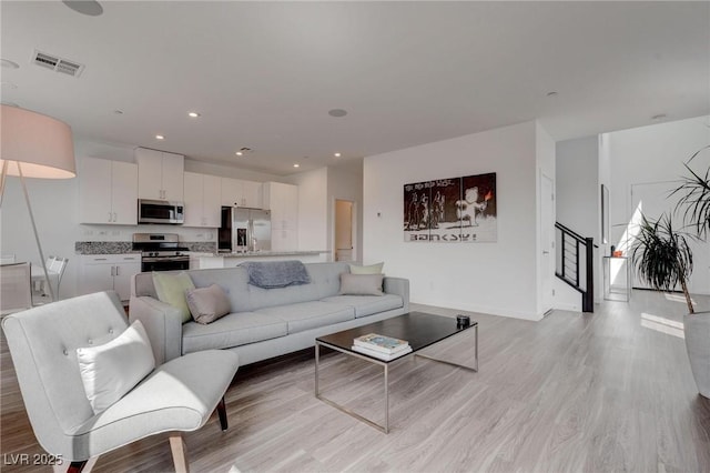 living area with light wood-type flooring, baseboards, visible vents, and stairs