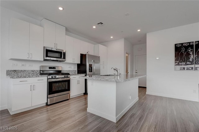 kitchen featuring visible vents, white cabinets, a sink, light wood finished floors, and stainless steel appliances