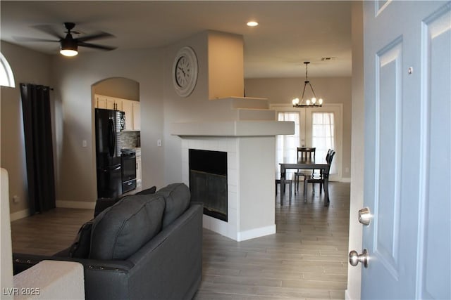 living room featuring baseboards, recessed lighting, a tiled fireplace, light wood finished floors, and ceiling fan with notable chandelier