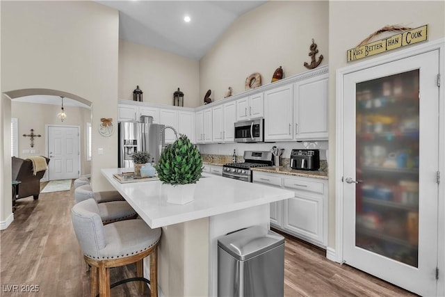 kitchen featuring high vaulted ceiling, arched walkways, appliances with stainless steel finishes, and a kitchen breakfast bar