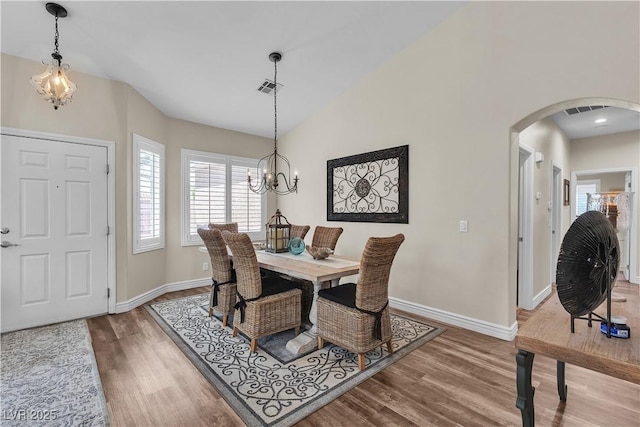 dining area featuring baseboards, wood finished floors, arched walkways, and a chandelier