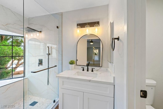bathroom featuring ceiling fan, toilet, vanity, and a marble finish shower