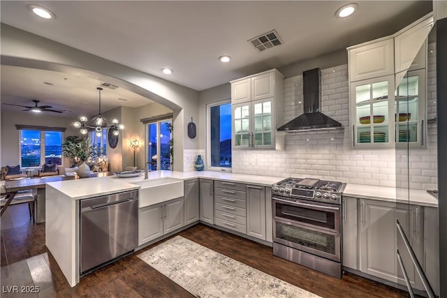 kitchen featuring wall chimney range hood, visible vents, gray cabinets, appliances with stainless steel finishes, and a sink