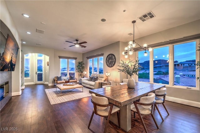 dining room with dark wood-style flooring, baseboards, a fireplace, visible vents, and arched walkways