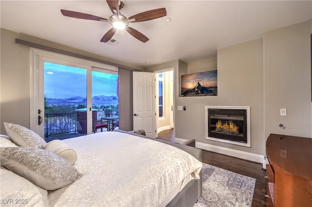 bedroom with a glass covered fireplace, baseboards, dark wood-style floors, visible vents, and ceiling fan