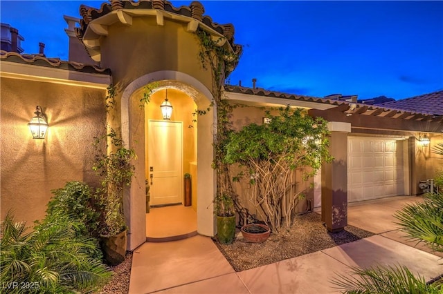 view of exterior entry featuring an attached garage, driveway, and stucco siding