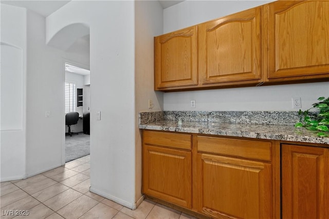3024 Pismo Beach Dr, Las Vegas, NV 89128 - kitchen with light stone countertops, light tile patterned flooring, baseboards, and arched walkways