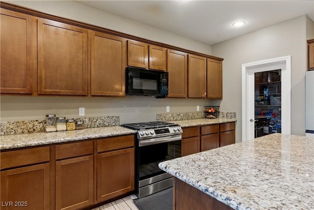 kitchen featuring black microwave, stainless steel gas range oven, and brown cabinets