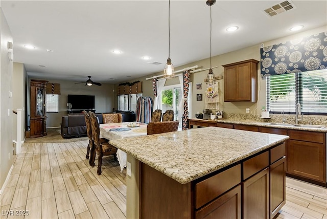 kitchen featuring visible vents, a ceiling fan, a kitchen island, a sink, and hanging light fixtures