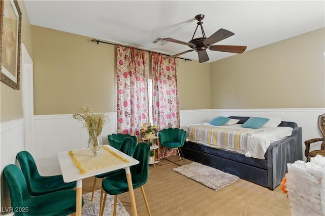 carpeted bedroom with ceiling fan, wainscoting, and visible vents