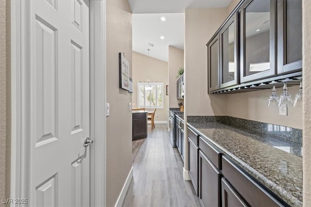 kitchen with glass insert cabinets, dark brown cabinets, dark stone counters, baseboards, and light wood-style floors