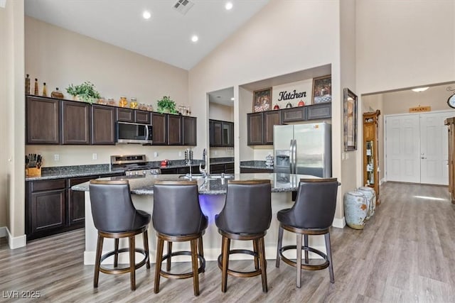 kitchen with dark brown cabinets, visible vents, a sink, high vaulted ceiling, and stainless steel appliances