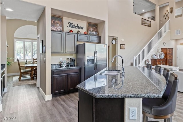 kitchen with a sink, dark stone counters, stainless steel refrigerator with ice dispenser, light wood-style flooring, and baseboards