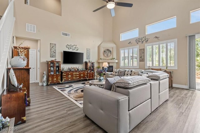 living area featuring a high ceiling, a ceiling fan, visible vents, and light wood-style floors