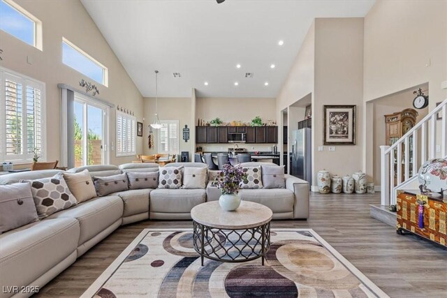 living room with recessed lighting, stairway, light wood finished floors, and high vaulted ceiling