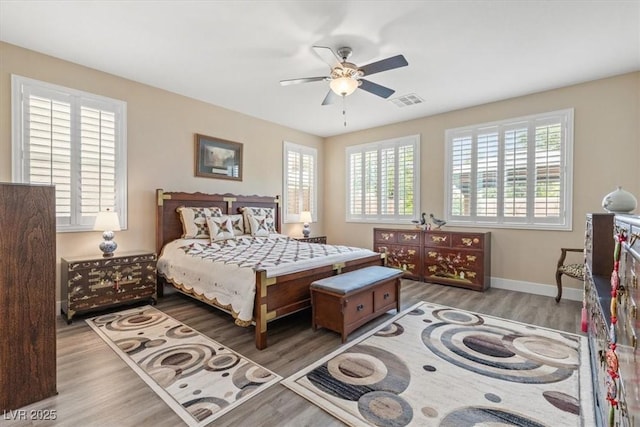 bedroom with baseboards, multiple windows, visible vents, and wood finished floors