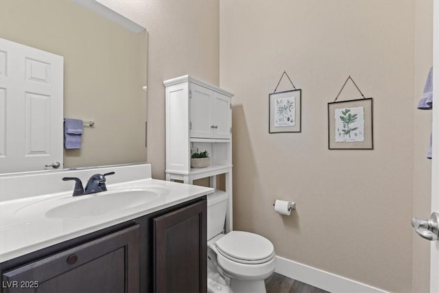 half bath with baseboards, vanity, toilet, and wood finished floors