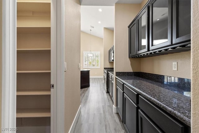 4212 Hawks Glide Ave, North Las Vegas, NV 89084 - kitchen with light wood-style flooring, dark cabinetry, stainless steel microwave, dark stone countertops, and a chandelier