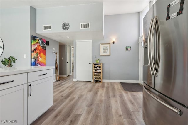 kitchen featuring stainless steel refrigerator with ice dispenser, light wood-type flooring, visible vents, and white cabinetry