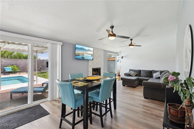 dining space featuring a fireplace, light wood-type flooring, and a ceiling fan