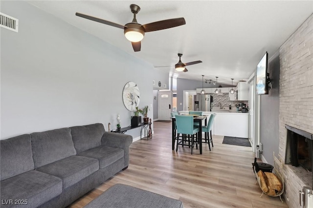 living room with visible vents, a stone fireplace, ceiling fan, light wood-type flooring, and vaulted ceiling