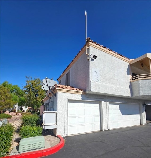 8452 Boseck Dr Unit 216, Las Vegas, NV 89145 - view of property exterior featuring a tile roof, stucco siding, an attached garage, and driveway
