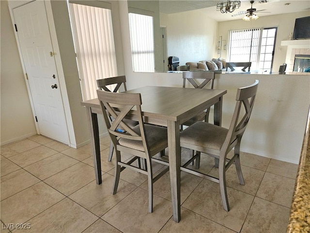 dining room featuring a tiled fireplace, light tile patterned floors, and baseboards