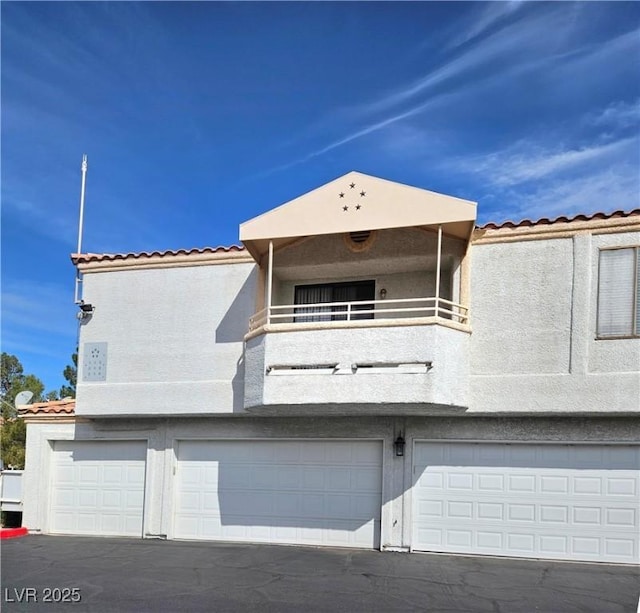 8452 Boseck Dr Unit 216, Las Vegas, NV 89145 - rear view of house featuring a balcony, a garage, a tiled roof, and stucco siding