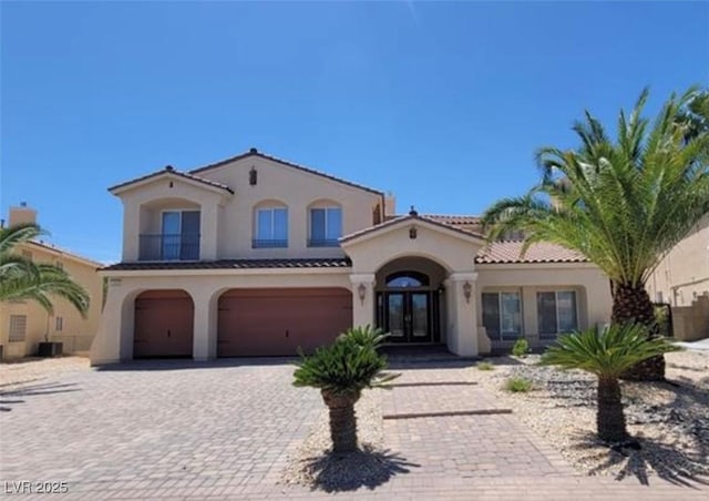 mediterranean / spanish-style home with french doors, a garage, stucco siding, and decorative driveway