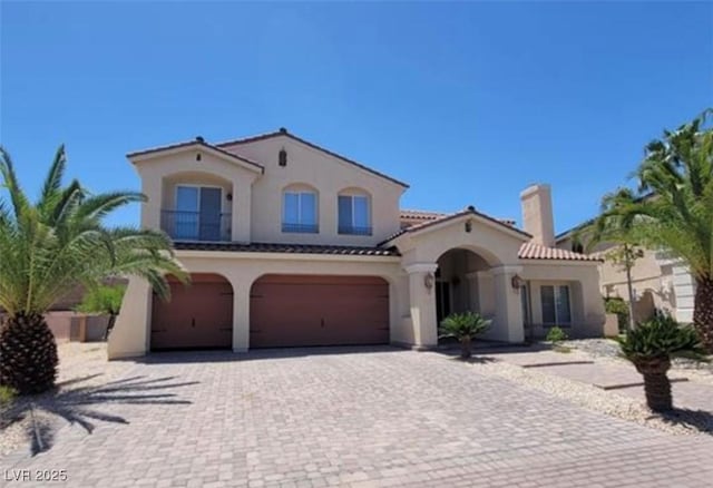 mediterranean / spanish-style house featuring a chimney, an attached garage, driveway, and stucco siding