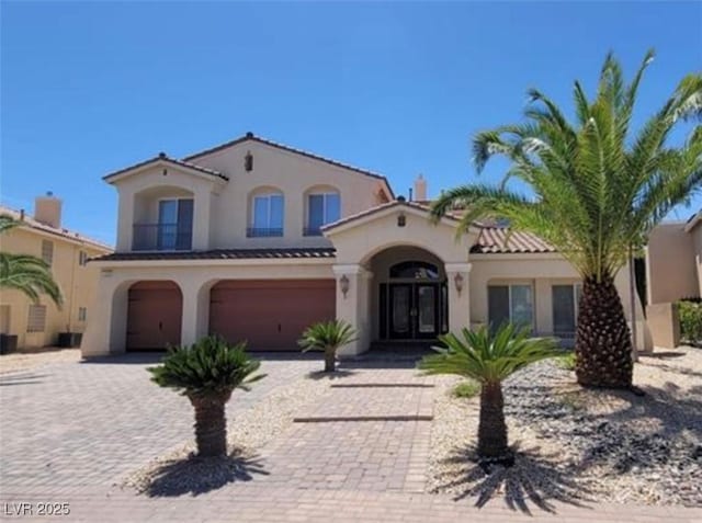 mediterranean / spanish-style house featuring stucco siding, driveway, french doors, an attached garage, and a tiled roof