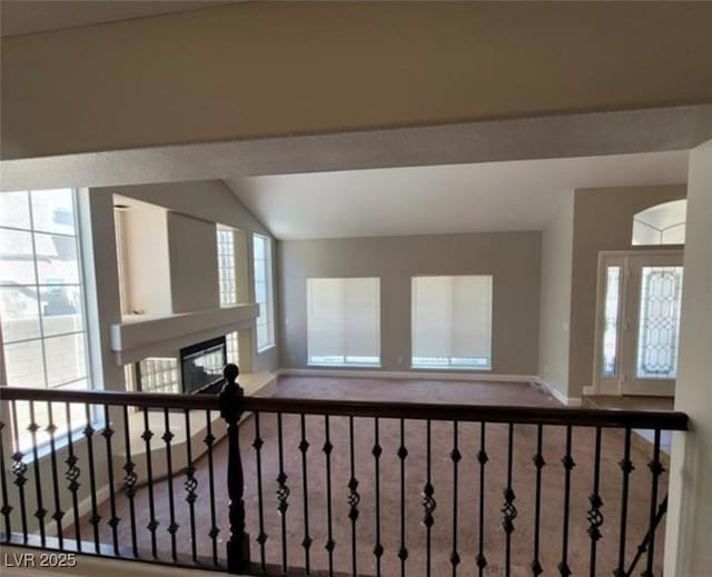 interior space featuring a glass covered fireplace, carpet, baseboards, and vaulted ceiling