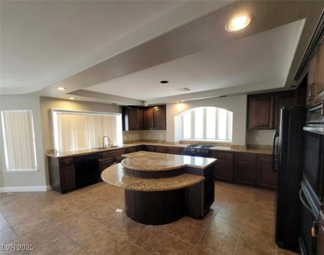 kitchen featuring a sink, dark brown cabinetry, a tray ceiling, black appliances, and a kitchen island