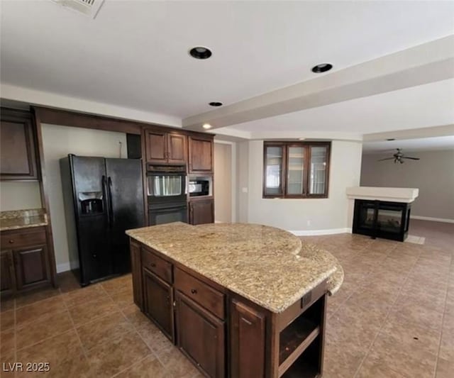 kitchen featuring a glass covered fireplace, light tile patterned floors, a center island, a ceiling fan, and black appliances