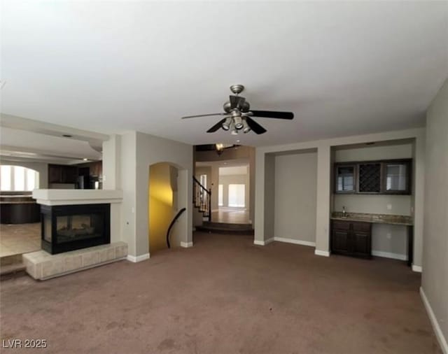 unfurnished living room with a multi sided fireplace, baseboards, stairway, and carpet flooring