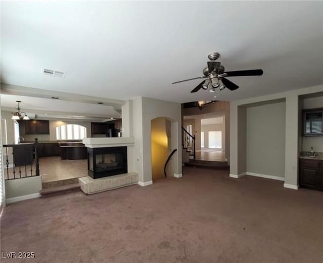 unfurnished living room featuring carpet floors, baseboards, visible vents, and stairway