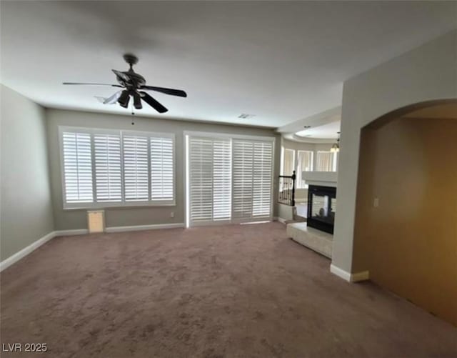 unfurnished living room featuring baseboards, a multi sided fireplace, a ceiling fan, arched walkways, and carpet