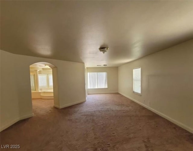 carpeted spare room featuring baseboards and arched walkways