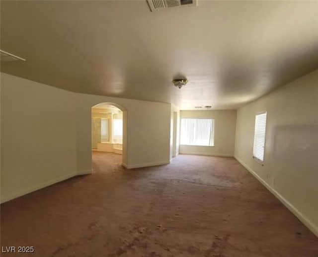 carpeted spare room featuring arched walkways, visible vents, and baseboards