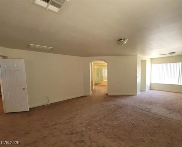 carpeted empty room with arched walkways, baseboards, and visible vents