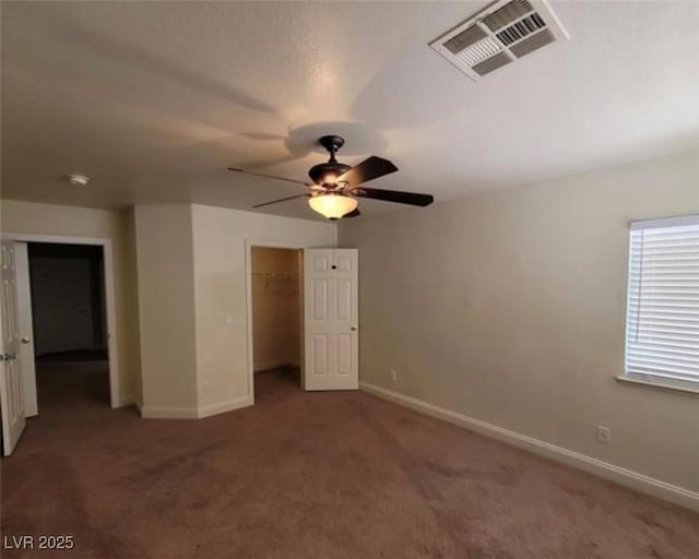 unfurnished bedroom featuring a closet, baseboards, carpet floors, a walk in closet, and visible vents
