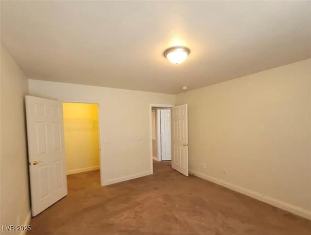 unfurnished bedroom with a spacious closet, carpet floors, baseboards, and a closet