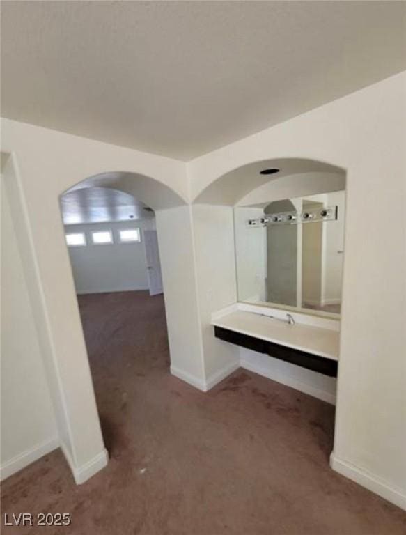 corridor with arched walkways, carpet flooring, and baseboards