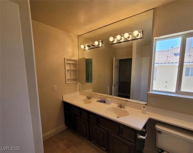 full bath featuring toilet, double vanity, a sink, and baseboards
